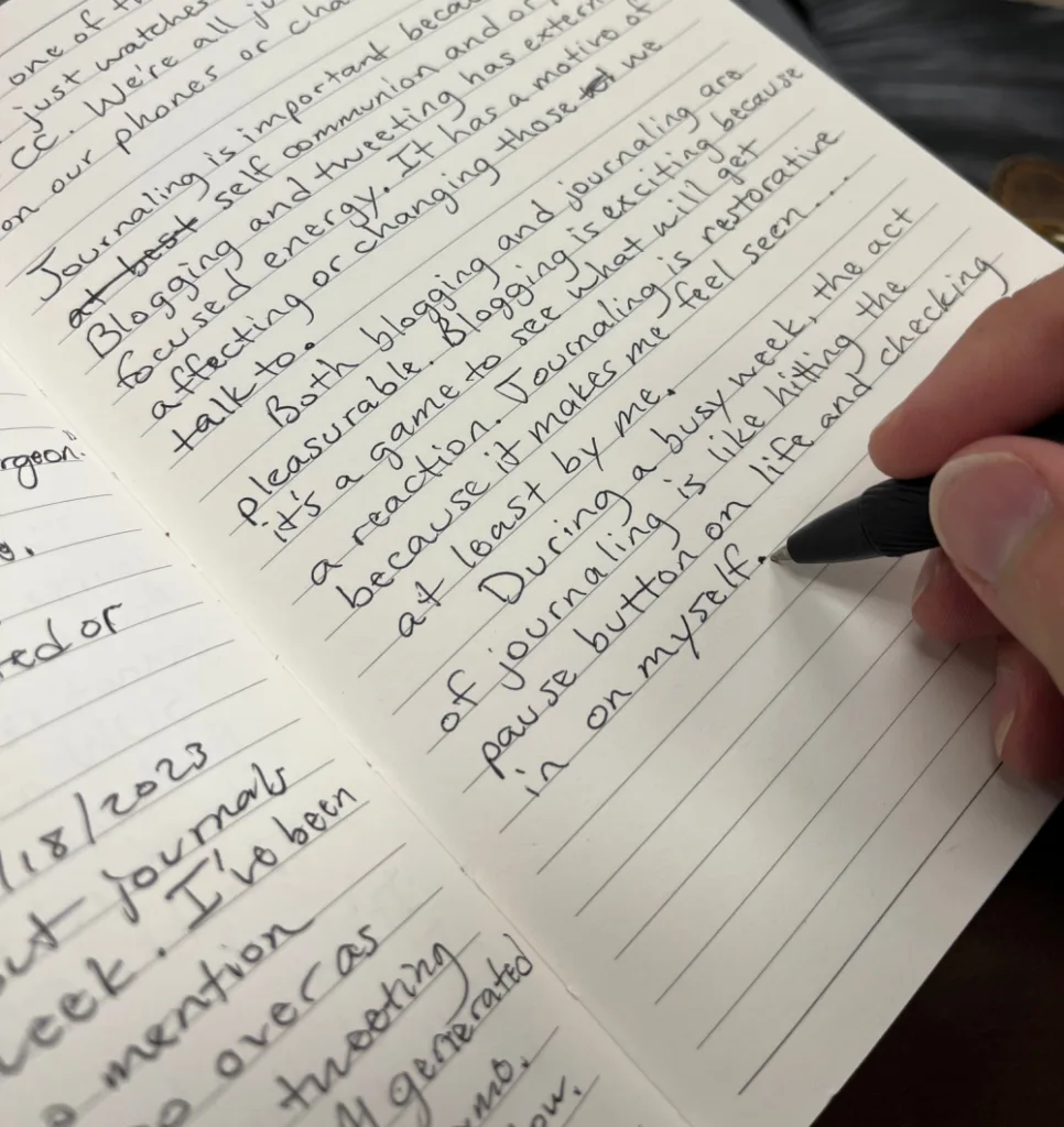 image of a hand holding a pen, writing in a journal about the difference between blogging and journaling