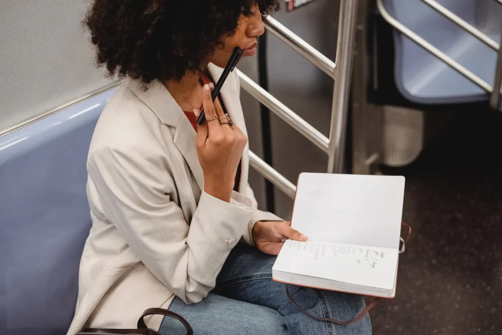woman sitting in a subway car writing in a journal.