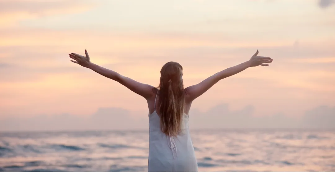 woman standing arms outstretched before the ocean at sunset