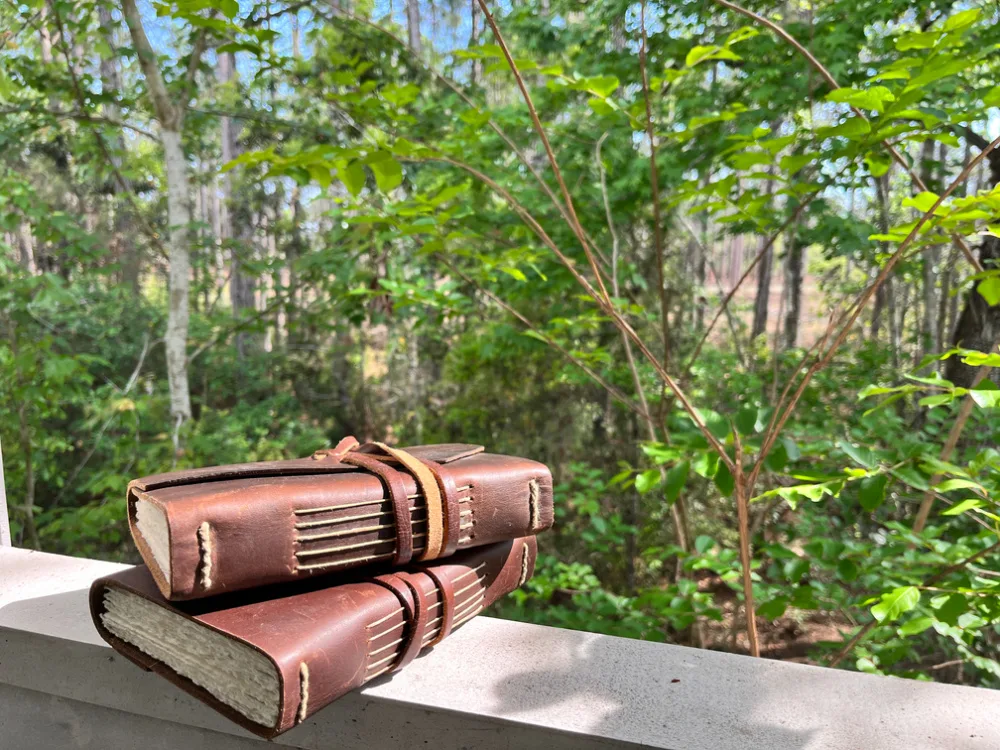 leather journals resting on a balcony railing overlooking the woods.